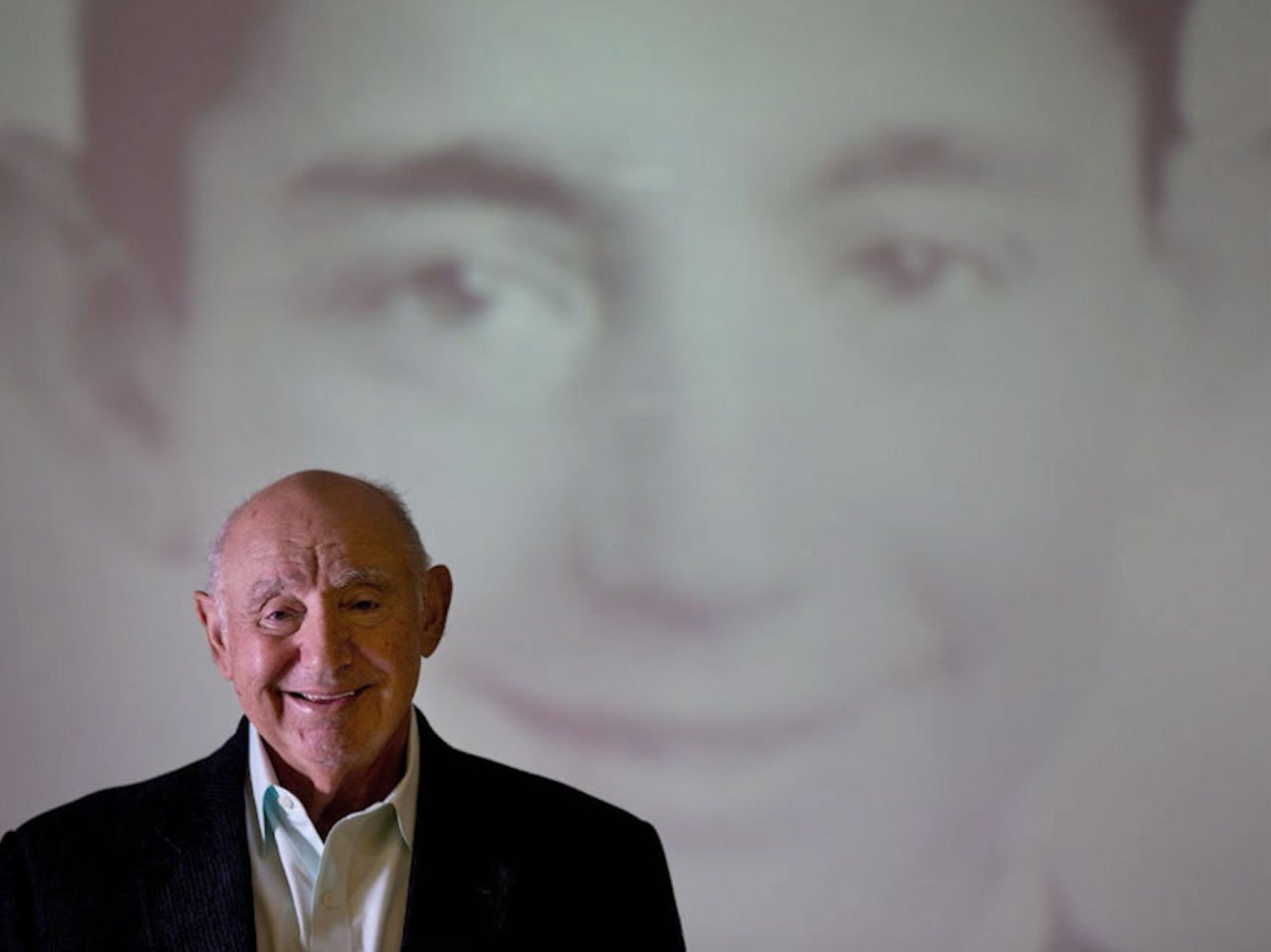 Milt Kleinberg in front of a picture of himself as a young man. He later wrote a book, Bread or Death, about his experiences during the Holocaust.